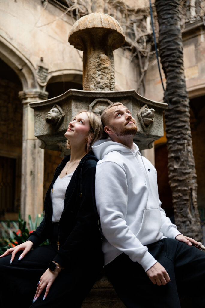 Para siedząca tyłem do siebie przy zabytkowej fontannie w Dzielnicy Gotyckiej w Barcelonie.