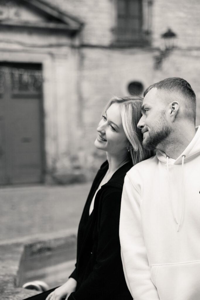 Roześmiana para oparta o siebie plecami przed zabytkowym budynkiem w Barcelonie.