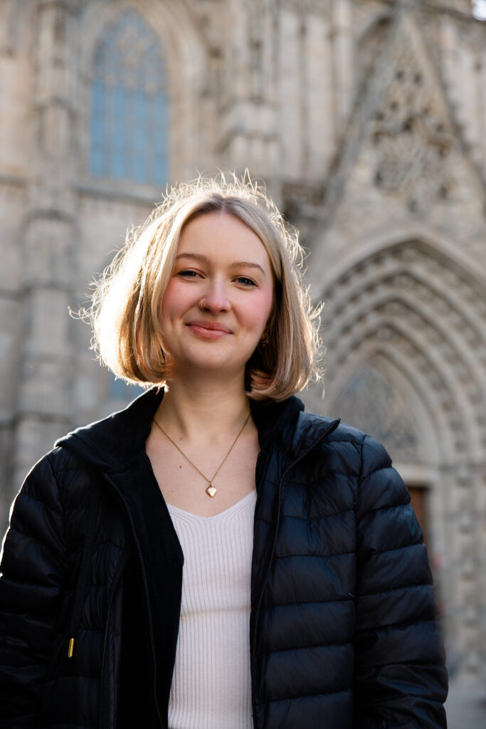 Portret uśmiechniętej blondynki na tle Katedry św. Eulalii w Barcelonie.