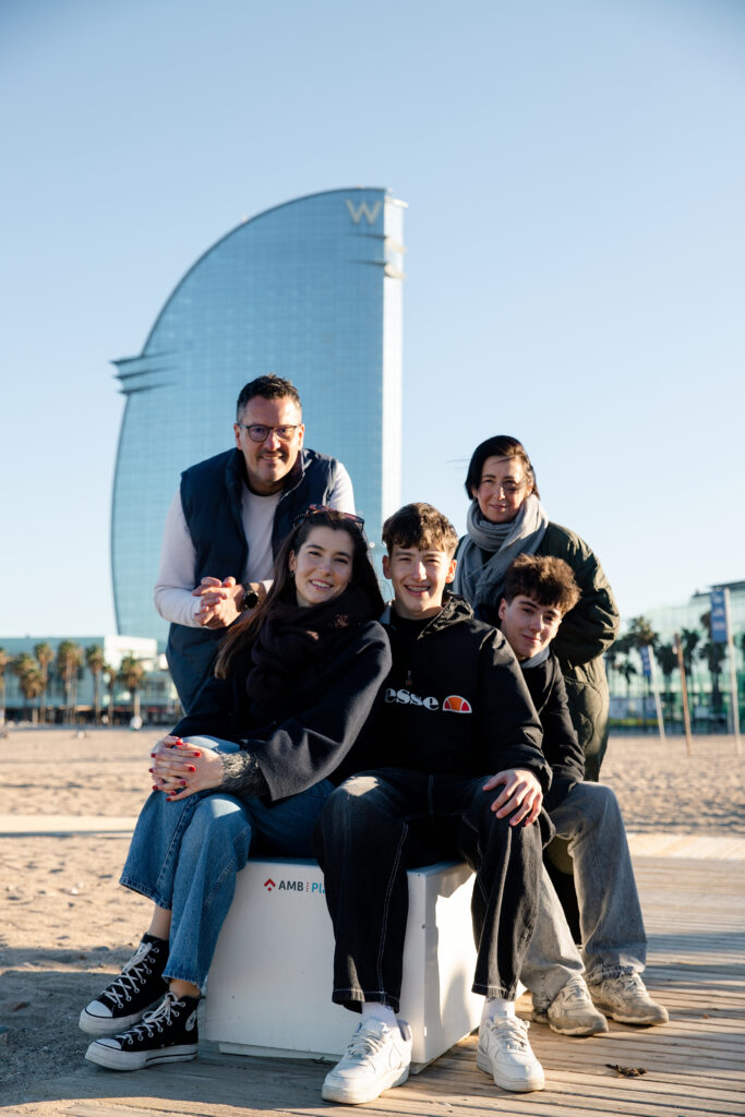 Uśmiechnięta rodzina na tle palm i hotelu W w porcie w Barcelonie.