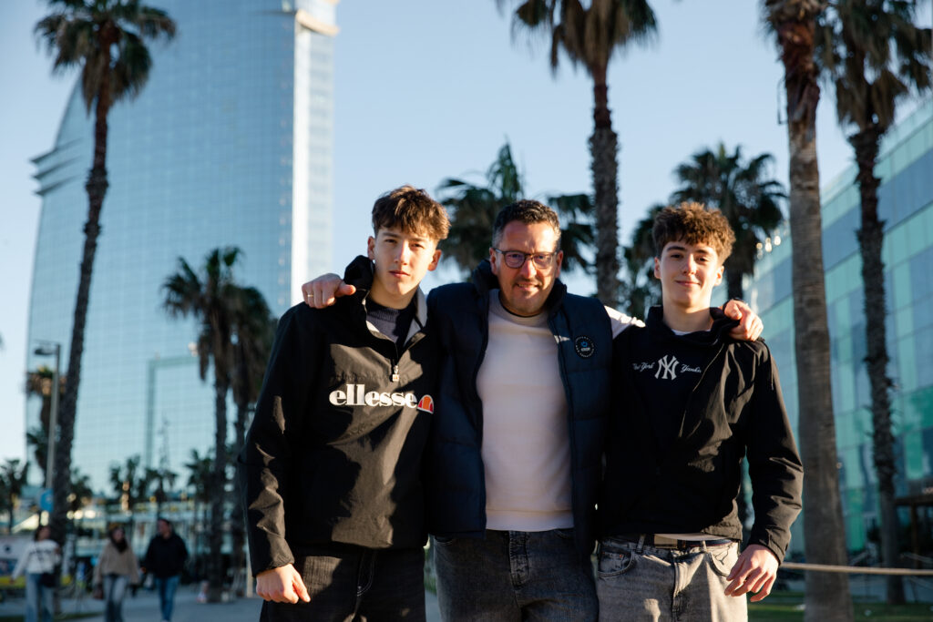 Uśmiechnięta rodzina na tle palm i jachtów w porcie w Barcelonie.